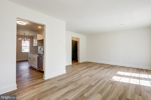 unfurnished living room with baseboards, light wood-style flooring, and a notable chandelier