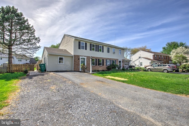 colonial home featuring brick siding, a front lawn, fence, and driveway