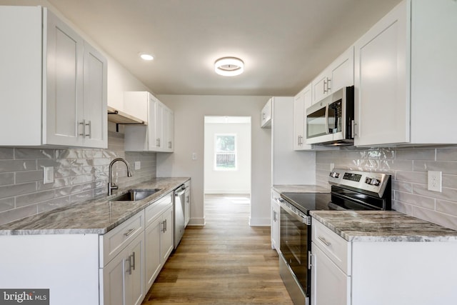 kitchen with appliances with stainless steel finishes, tasteful backsplash, a sink, baseboards, and white cabinetry