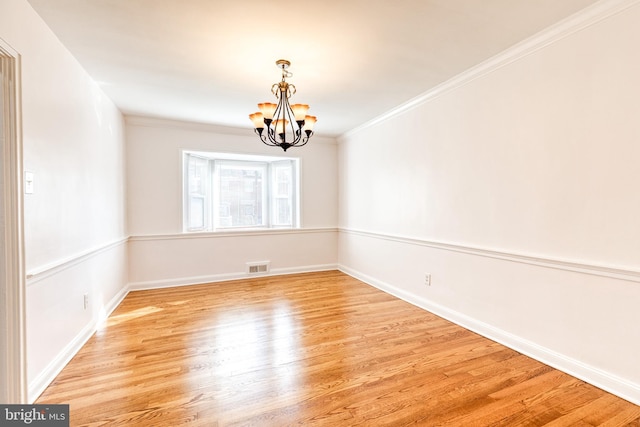 spare room featuring visible vents, crown molding, light wood-type flooring, baseboards, and a notable chandelier