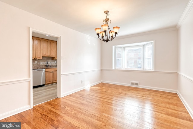unfurnished dining area featuring a sink, light wood finished floors, a chandelier, baseboards, and visible vents