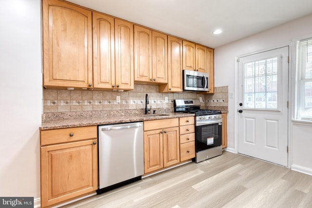 kitchen with light wood-style floors, tasteful backsplash, light stone counters, a sink, and appliances with stainless steel finishes
