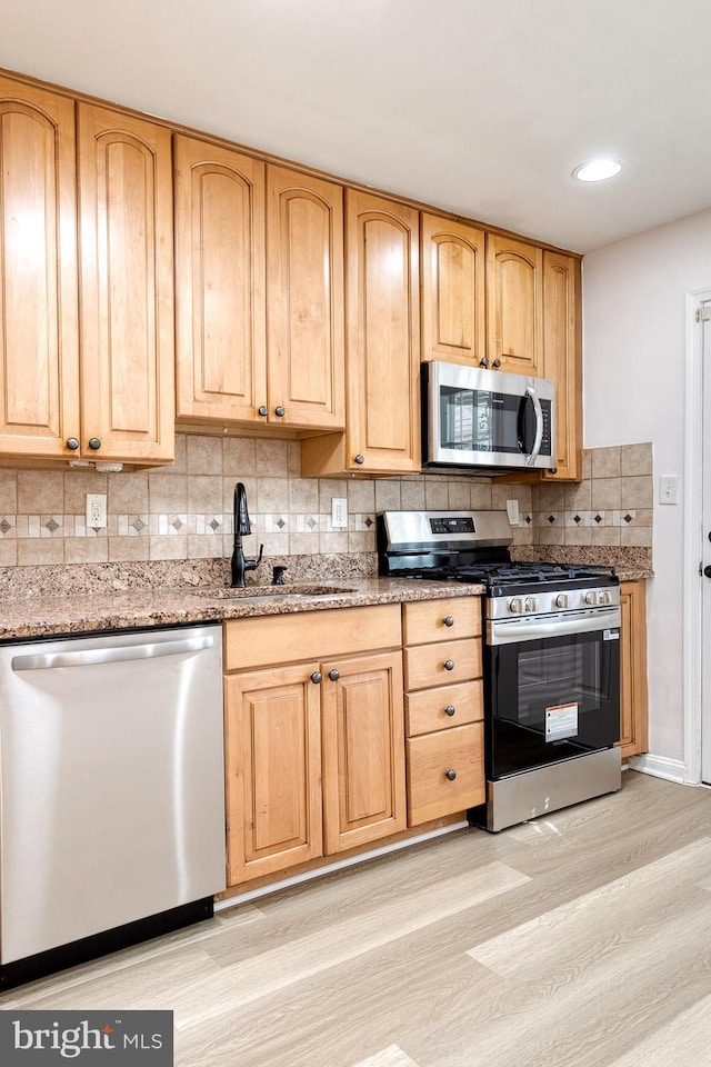 kitchen featuring light stone counters, a sink, light wood-style floors, stainless steel appliances, and tasteful backsplash
