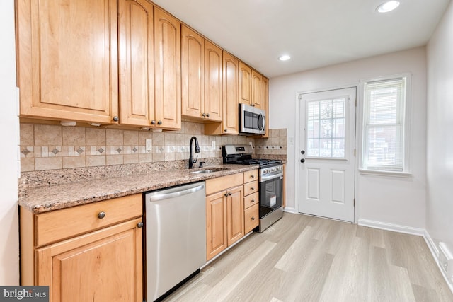 kitchen featuring light brown cabinetry, stainless steel appliances, a sink, and light wood finished floors