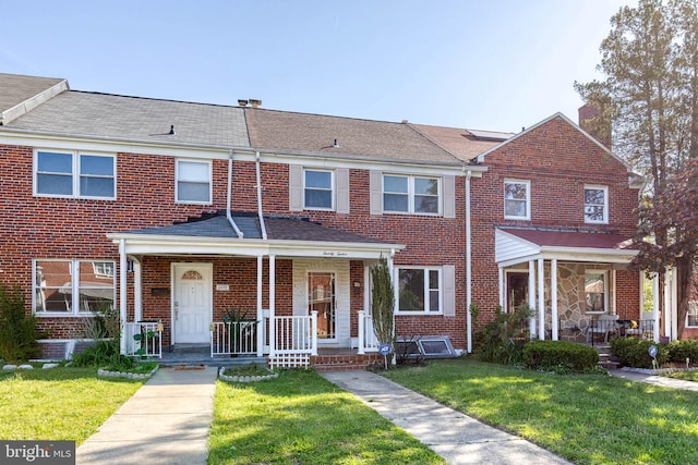 view of property with a porch, brick siding, a chimney, and a front lawn