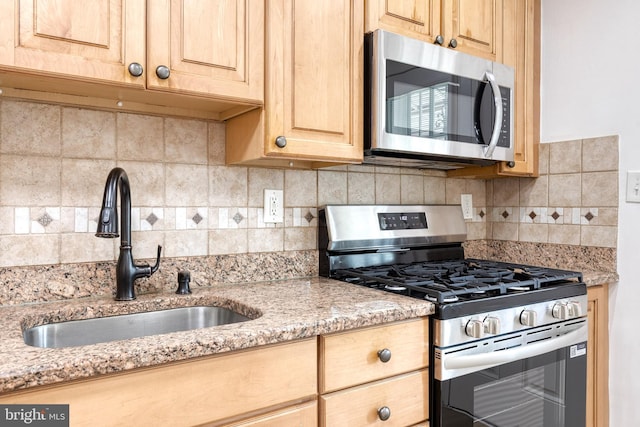 kitchen featuring light brown cabinets, appliances with stainless steel finishes, a sink, and tasteful backsplash