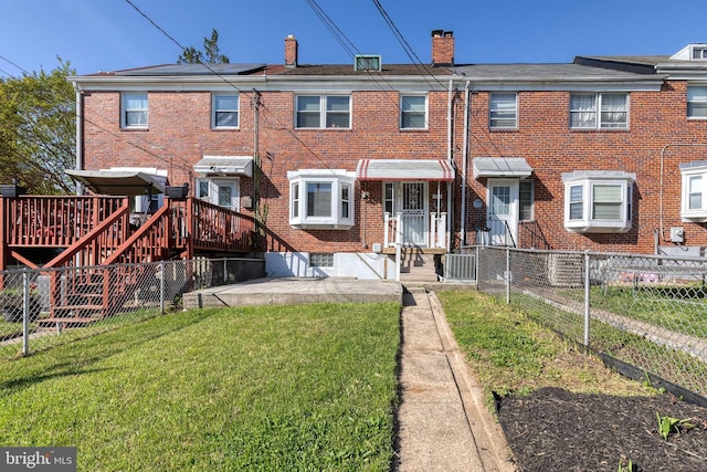 rear view of property with a wooden deck, fence, a chimney, brick siding, and a yard