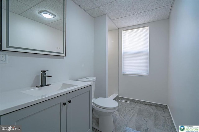 bathroom featuring walk in shower, vanity, baseboards, toilet, and a drop ceiling
