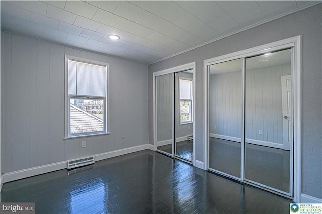 unfurnished bedroom with multiple closets, multiple windows, wood finished floors, and visible vents