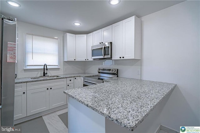 kitchen with appliances with stainless steel finishes, a sink, light stone counters, a peninsula, and white cabinetry