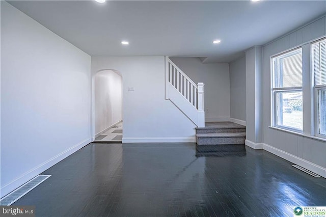 unfurnished living room with visible vents, stairs, wood finished floors, recessed lighting, and arched walkways