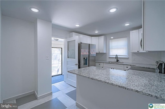 kitchen with light stone counters, a sink, electric stove, white cabinetry, and stainless steel refrigerator with ice dispenser