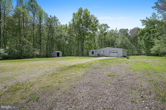 view of yard featuring an outdoor structure, driveway, a view of trees, a storage shed, and a detached garage