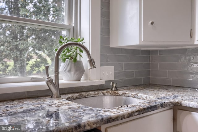 interior details featuring backsplash, stone countertops, white cabinets, and a sink