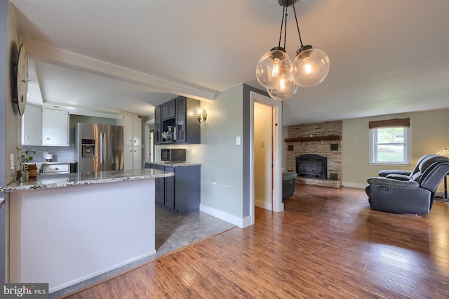 kitchen featuring stainless steel appliances, wood finished floors, light stone counters, open floor plan, and baseboards