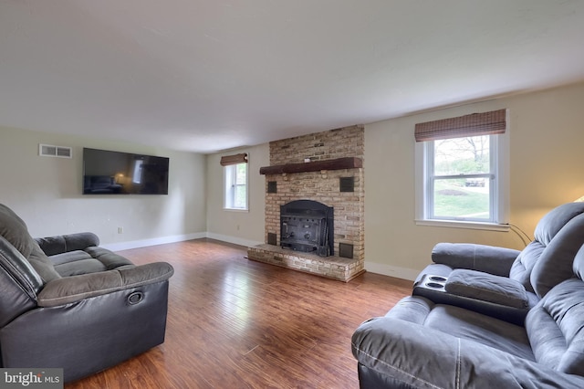living room with a brick fireplace, baseboards, visible vents, and wood finished floors