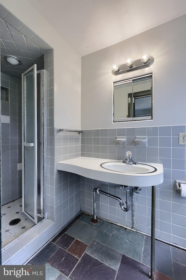 bathroom featuring tile walls, wainscoting, a shower stall, and stone tile flooring