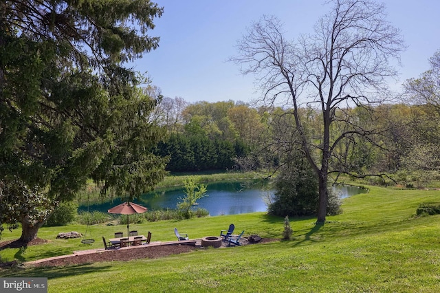 view of community featuring a fire pit, a water view, and a lawn