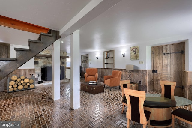 interior space with a wainscoted wall, wooden walls, brick floor, and stairs