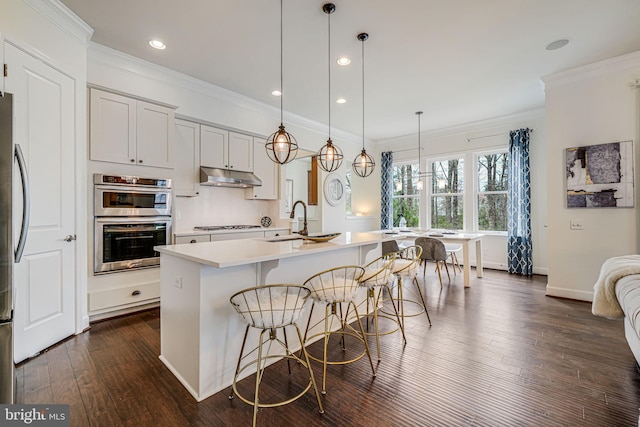 kitchen featuring under cabinet range hood, a sink, dark wood-style flooring, light countertops, and a kitchen bar