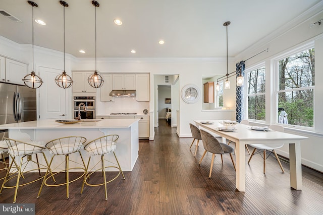 kitchen with under cabinet range hood, gas stovetop, stainless steel refrigerator, baseboards, and light countertops