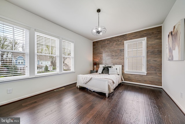 bedroom featuring a chandelier, wood walls, an accent wall, dark wood finished floors, and baseboards