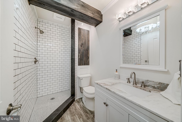 bathroom featuring toilet, wood finished floors, tiled shower, vanity, and ornamental molding