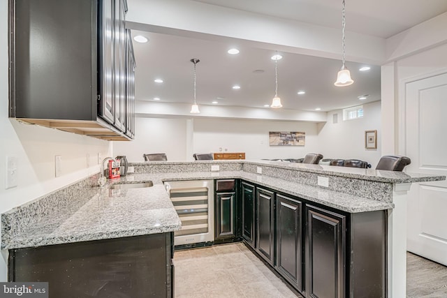 kitchen with wine cooler, a sink, light stone counters, dark cabinetry, and recessed lighting