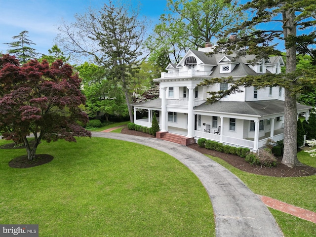 view of front facade featuring a front lawn, a balcony, covered porch, and a chimney