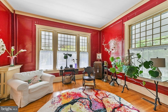 living area featuring crown molding, visible vents, wood finished floors, and a decorative wall