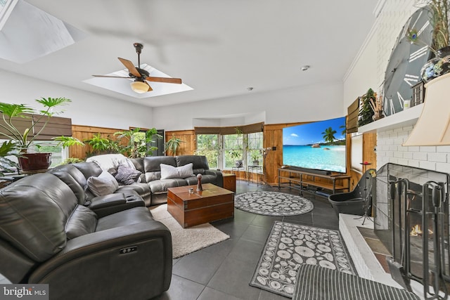 living area featuring a ceiling fan, a fireplace, tile patterned floors, and a skylight