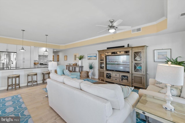 living area featuring crown molding, ceiling fan, light wood finished floors, and visible vents