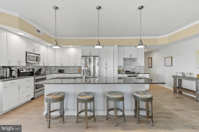 kitchen with crown molding, a breakfast bar, an island with sink, tasteful backsplash, and stainless steel appliances