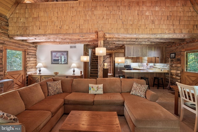 living area featuring stairs, a high ceiling, log walls, and beam ceiling