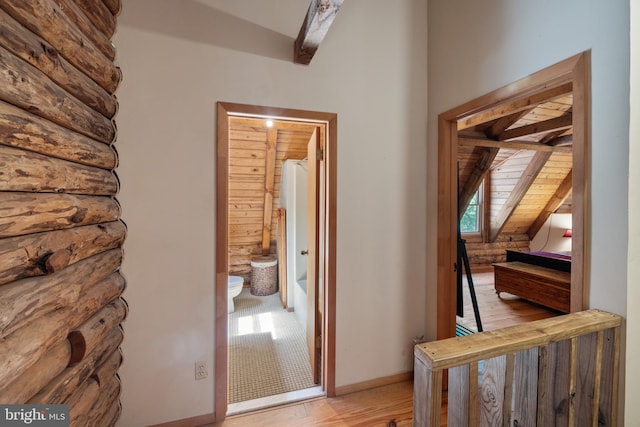 corridor with vaulted ceiling with beams, rustic walls, and light wood finished floors