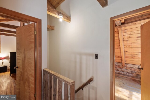 corridor featuring beamed ceiling, an upstairs landing, and hardwood / wood-style flooring