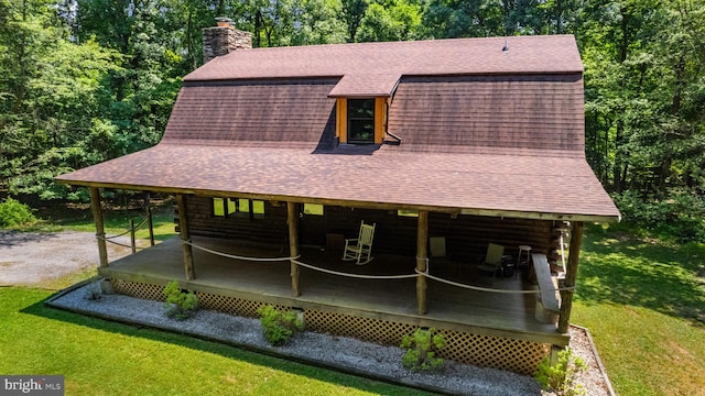exterior space featuring roof with shingles, a wooden deck, a chimney, and a front lawn