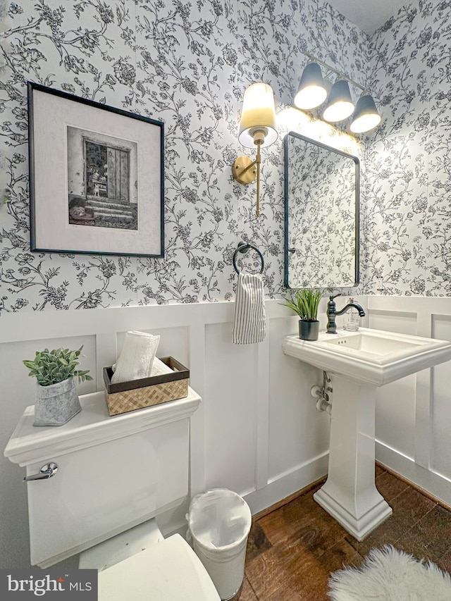 half bath featuring a decorative wall, toilet, wallpapered walls, and a wainscoted wall