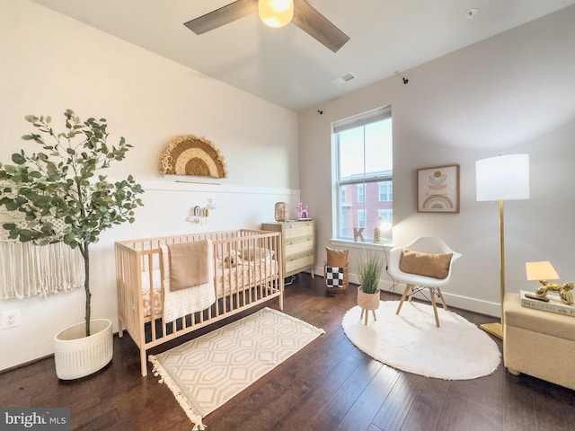 bedroom with ceiling fan, visible vents, a crib, and wood finished floors