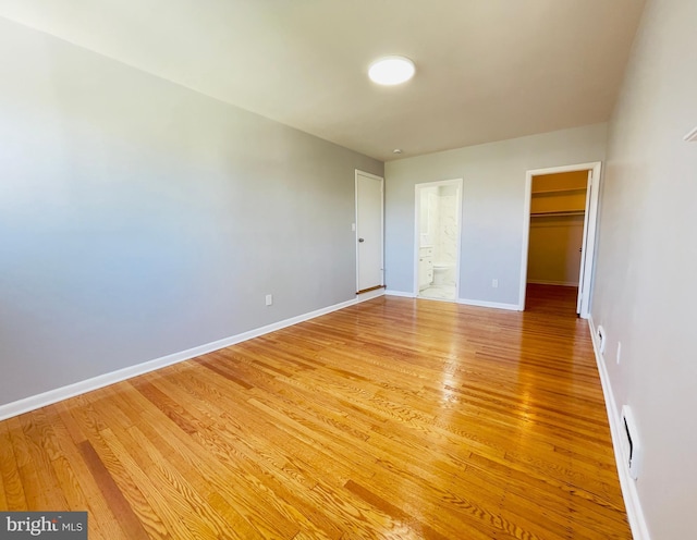 unfurnished bedroom featuring light wood finished floors, ensuite bath, baseboards, a spacious closet, and a closet