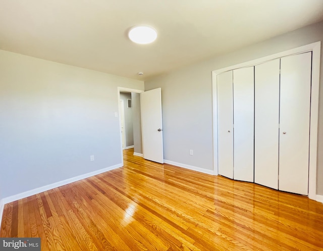 unfurnished bedroom with baseboards, light wood-style flooring, and a closet