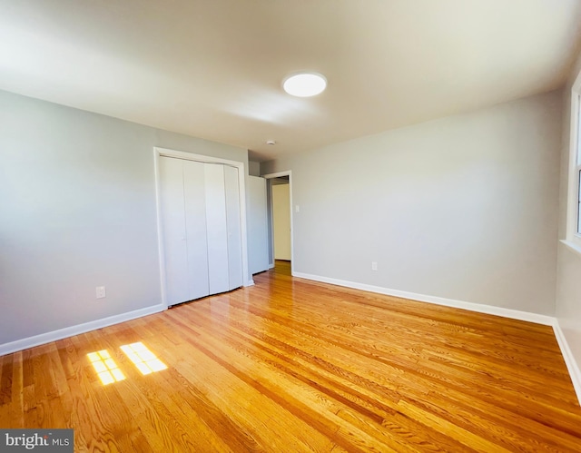 unfurnished bedroom featuring baseboards, light wood-style flooring, and a closet