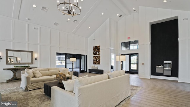 living area with visible vents, beam ceiling, high vaulted ceiling, an inviting chandelier, and a decorative wall