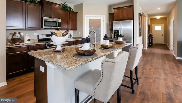 kitchen featuring dark wood-style flooring, a center island with sink, light stone countertops, and stainless steel appliances