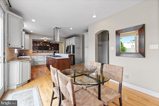 dining area featuring light wood-style flooring, arched walkways, recessed lighting, and baseboards