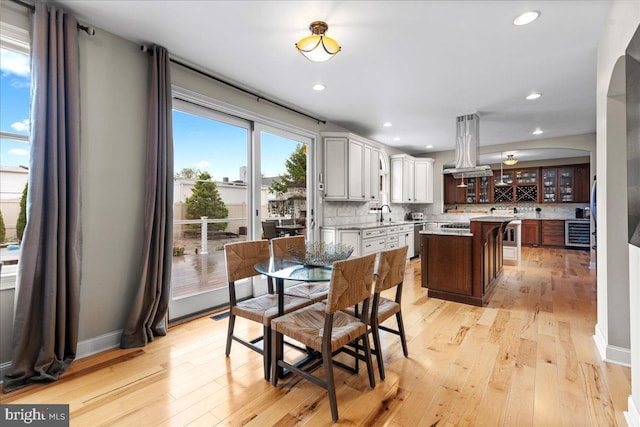 dining room featuring arched walkways, light wood-type flooring, recessed lighting, and beverage cooler