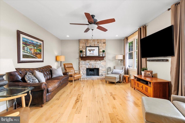 living room with ceiling fan, light wood-style flooring, a stone fireplace, and recessed lighting