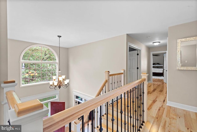 corridor with an upstairs landing, a chandelier, wood finished floors, and baseboards