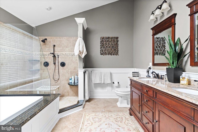 bathroom with tiled shower, tile patterned floors, toilet, vaulted ceiling, and wainscoting