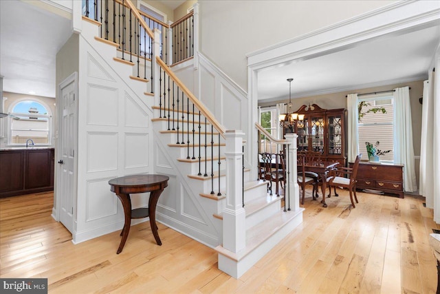 staircase featuring a decorative wall, healthy amount of natural light, a chandelier, wood-type flooring, and ornamental molding